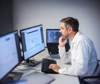 Denkströme IT-Spezialist arbeitet konzentriert an mehreren Monitoren – Softwareentwicklung und Programmierung im modernen Büro