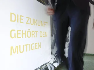 Person geht dynamisch an Wand mit motivierendem Schriftzug ‚Die Zukunft gehört den Mutigen‘ im Denkströme Büro vorbei