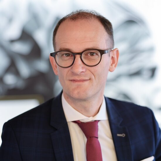 Portrait von Fabian Schmid, Geschäftsführer der Denkströme Gruppe, im Business-Outfit mit roter Krawatte – moderne Führungspersönlichkeit im Bereich Kommunikation und Transformation