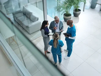 Multidisziplinäres Team aus medizinischem Fachpersonal und Verwaltungskräften im Gespräch in einem modernen Klinikgebäude – symbolisiert Zusammenarbeit, Gesundheitsmanagement und interprofessionellen Austausch im Gesundheitswesen